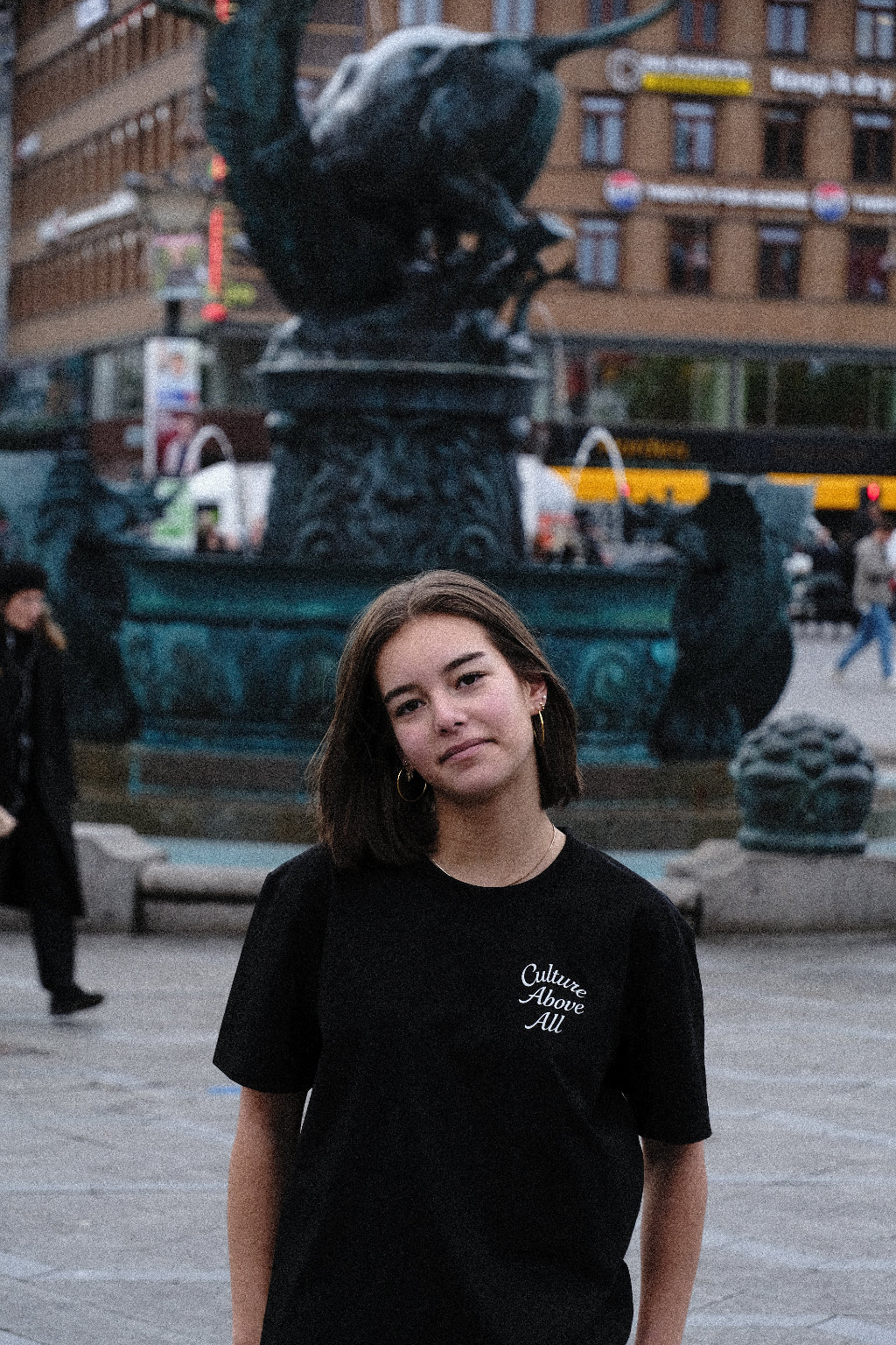 Person wearing a black t-shirt with text, standing on a street with blurred background