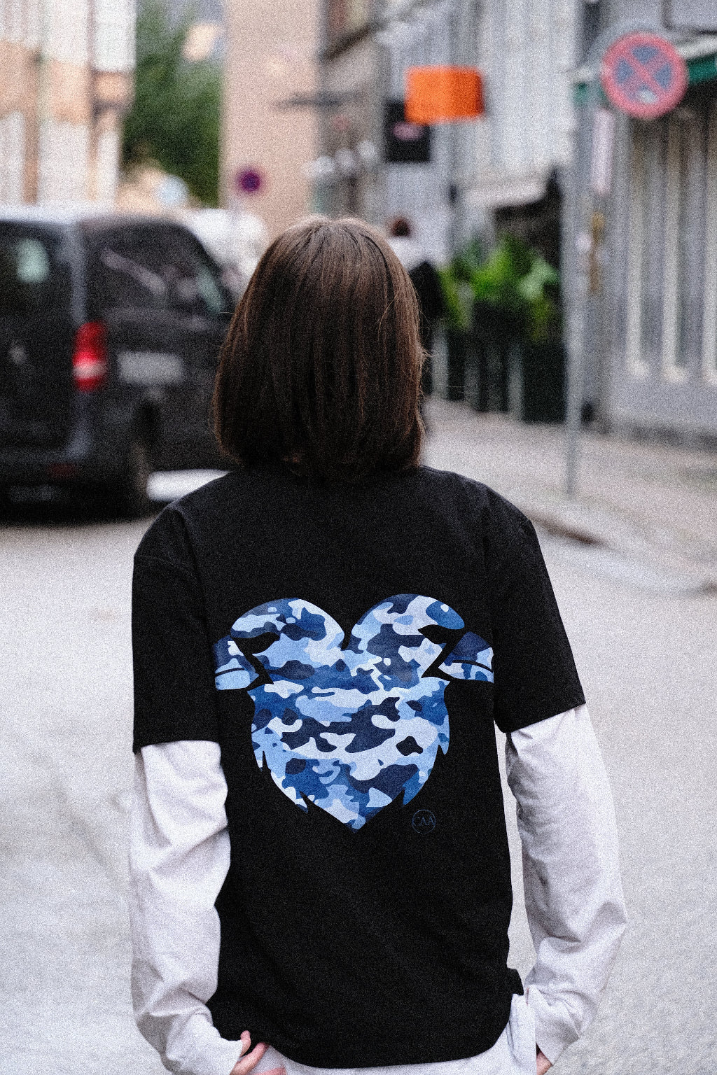 Person wearing a black jacket with a blue camouflage design, standing in an urban setting.